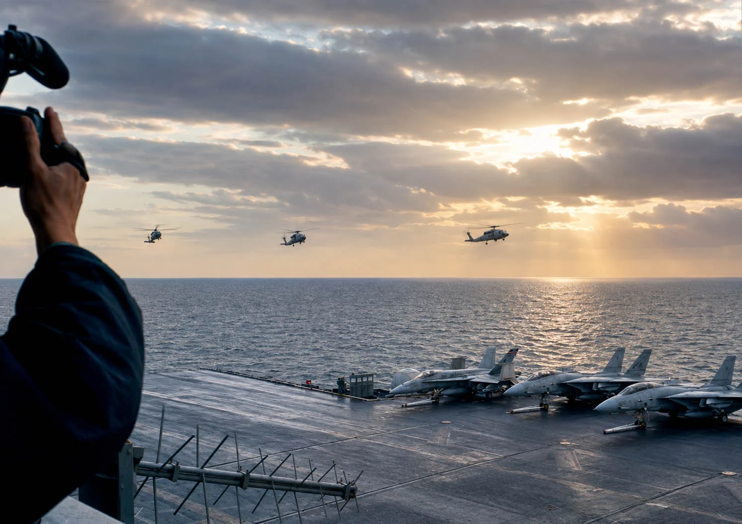 At the edge of the flight deck are an F/A-18 Hornet and a pair of F-14 Tomcats. In the background, three HH-60H Seahawk helicopters are approaching for landing.